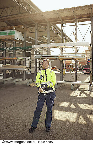 Mature female blue-collar worker in protective workwear standing outside factory