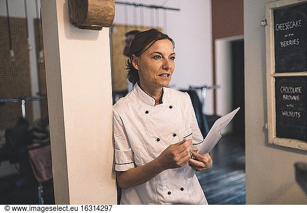 Mature female chef looking away while standing in restaurant