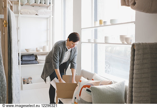 Mature female craftsperson unpacking products from cardboard box in store