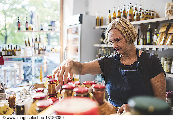 Mature female employee arranging jars in deli