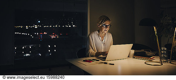 Mature female professional working late while using laptop at illuminated desk in office