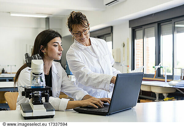 Mature female scientist and young colleague discussing over laptop at laboratory