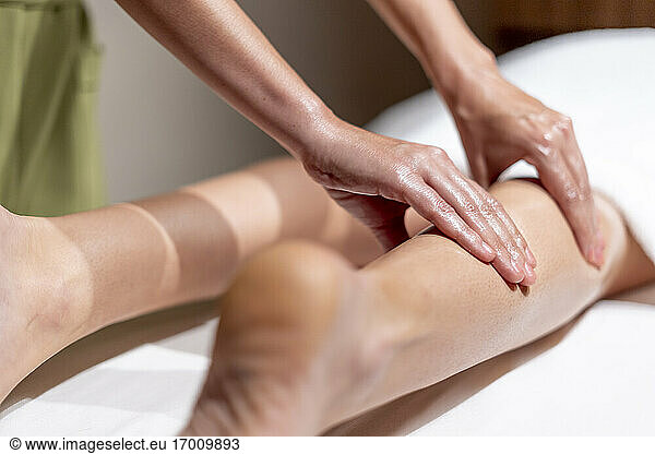 Mature female therapist massaging woman's leg at table in health spa