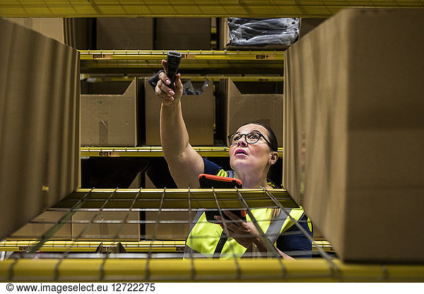 Mature female worker holding digital tablet and bar code reader against rack at distribution warehouse