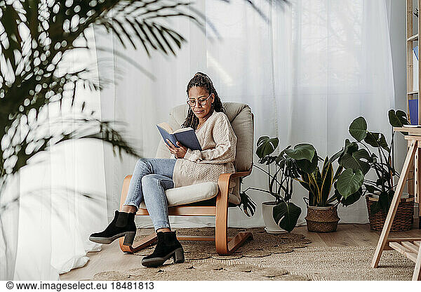 Mature freelancer reading book sitting on armchair at home office