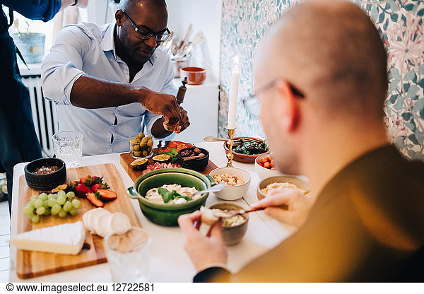 Mature friends with shaved head having food while sitting at table