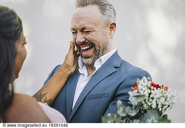 Mature groom laughing while looking at bride against wall