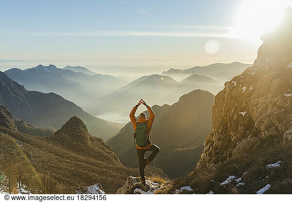 Mature hiker practicing tree pose on rock in front of mountains