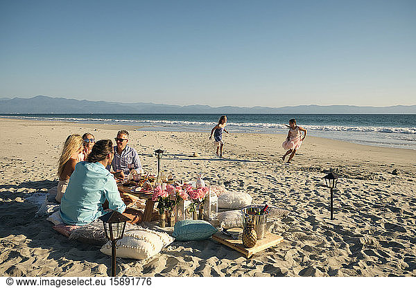 Mature male and female friends enjoying picnic while girls playing at beach against clear sky during sunny day. Riviera Nayarit,  Mexico