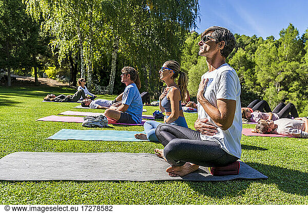 Mature male and female tourists practicing yoga on mat at health retreat during sunny day