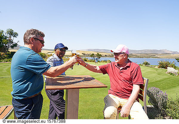 Mature male golfers drinking beer on sunny golf clubhouse patio