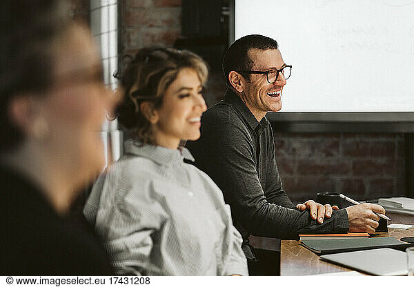 Mature male professional laughing while siting by female colleagues in board room