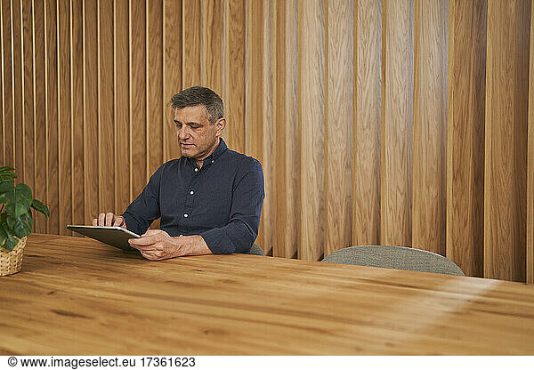 Mature male professional using digital tablet while sitting at conference table