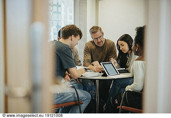 Mature male professor explaining students at table in university