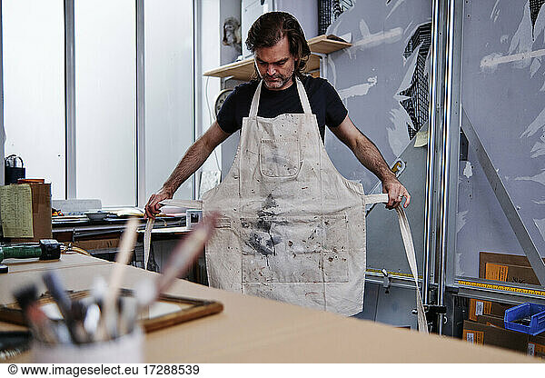 Mature male store owner wearing apron while standing in workshop