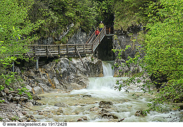Mature man and woman moving down on wooden staircase over waterfall near mountains