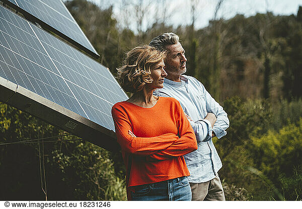 Mature man and woman standing with arms crossed by solar panels