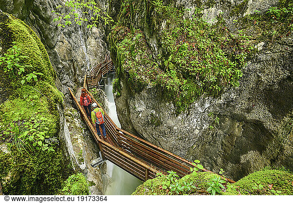 Mature man and woman walking on bridge over waterfall near mountains