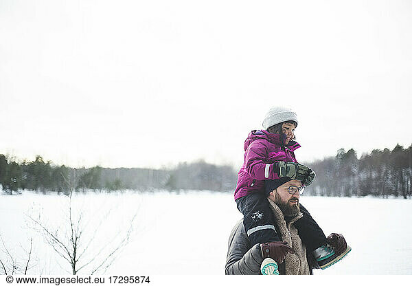Mature man carrying daughter on shoulders during winter
