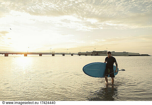 Mature man carrying paddleboard while walking in sea