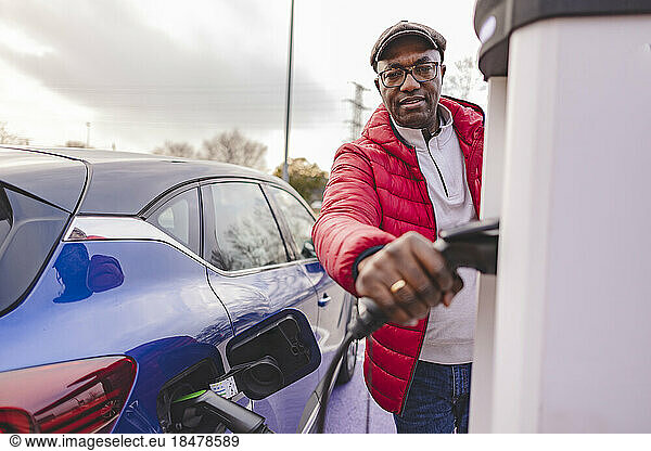 Mature man charging electric car at station