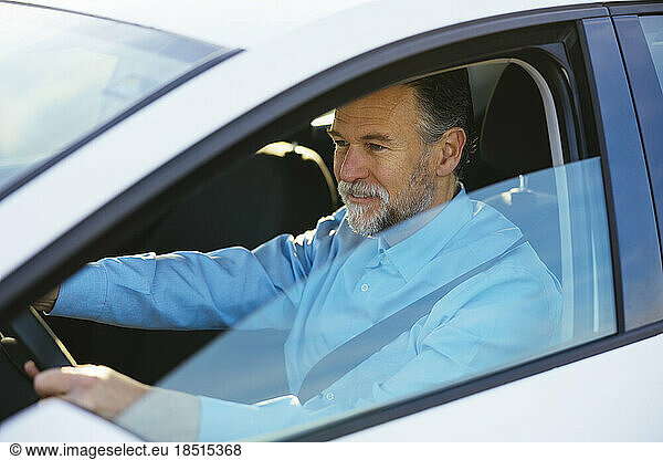 Mature man driving car seen through window