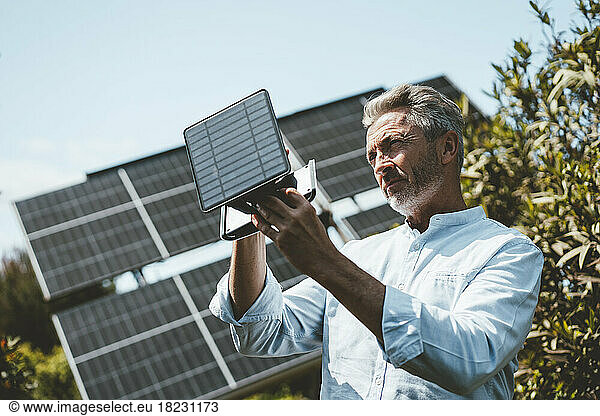 Mature man examining solar panel equipment on sunny day
