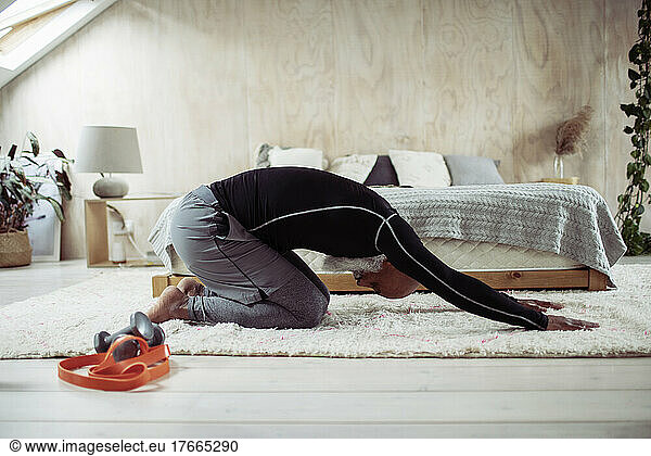 Mature man exercising in yoga childs pose on bedroom floor