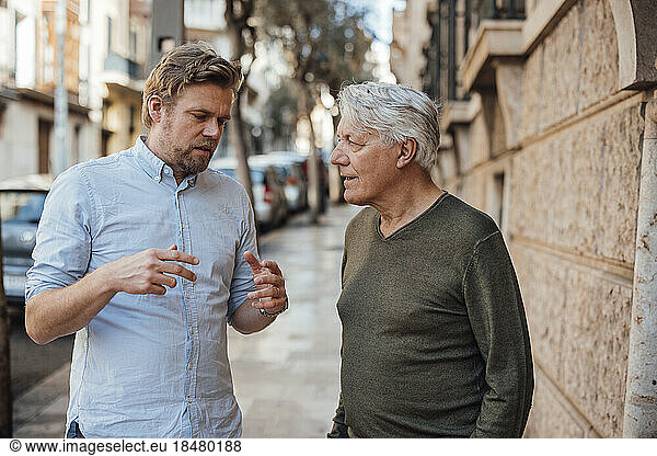 Mature man gesturing and having discussion with father standing on footpath