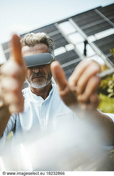 Mature man gesturing with VR glasses in front of solar panels