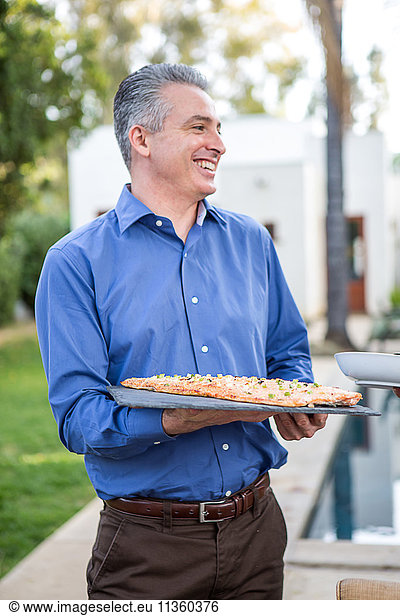 Mature man holding fish cuisine on cutting board at garden party