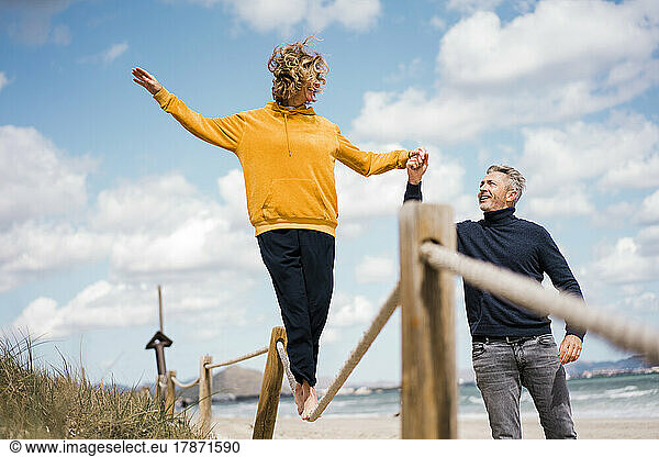 Mature man holding hand of woman assisting her walking on rope at beach