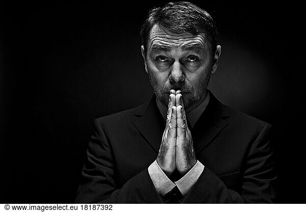 Mature man in full suit praying against black background  close up