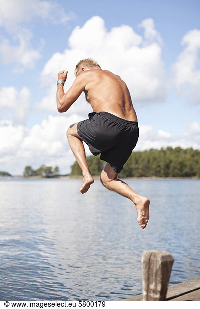 Mature man jumping into lake on sunny day