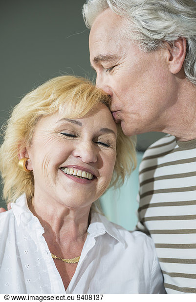 Mature man kissing mature woman on forehead  smiling