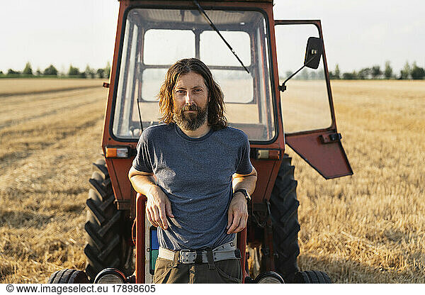 Mature man leaning on tractor at farm