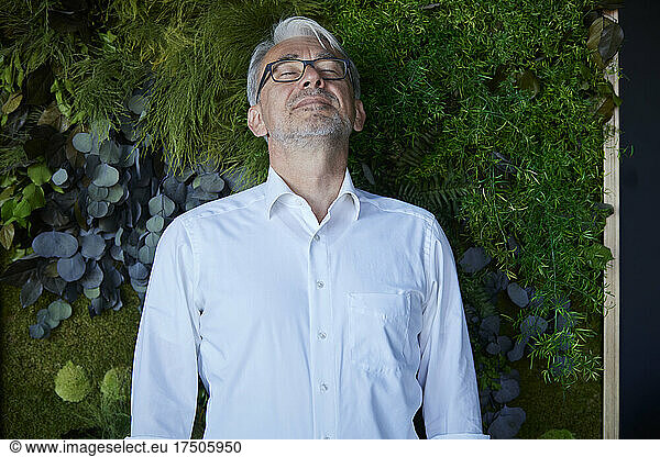 Mature man leaning with eyes closed on plant wall
