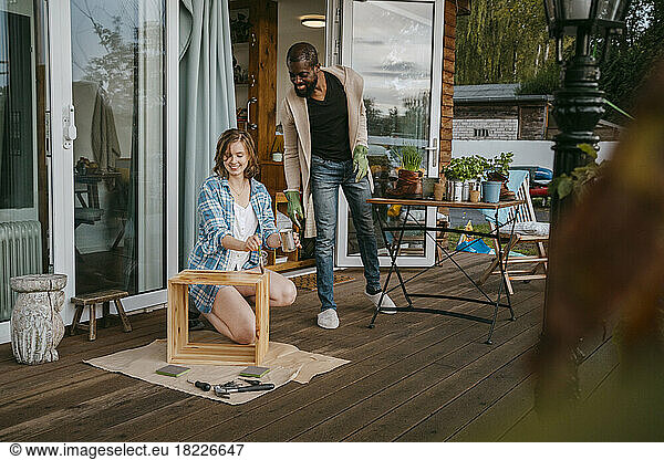 Mature man looking at woman painting furniture on porch outside house