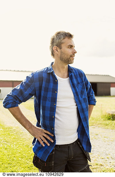 Mature man looking away while standing with hand on hip at farm