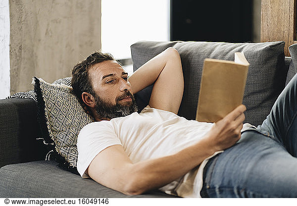 Mature man lying on couch  reading book