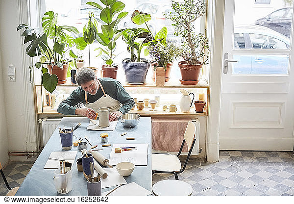 Mature man making craft product at table in pottery class
