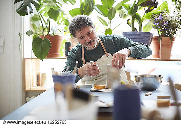 Mature man making craft product in pottery class