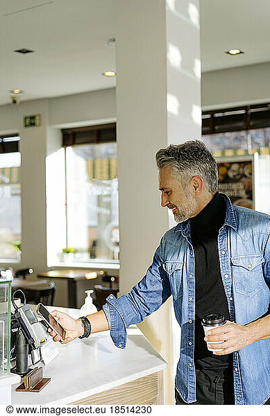 Mature man making payment through smart phone in cafe