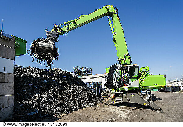 Mature man operating excavator and lifting rubber waste at recycling center