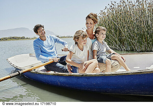 Mature man paddling while sitting with family in rowboat on sunny day
