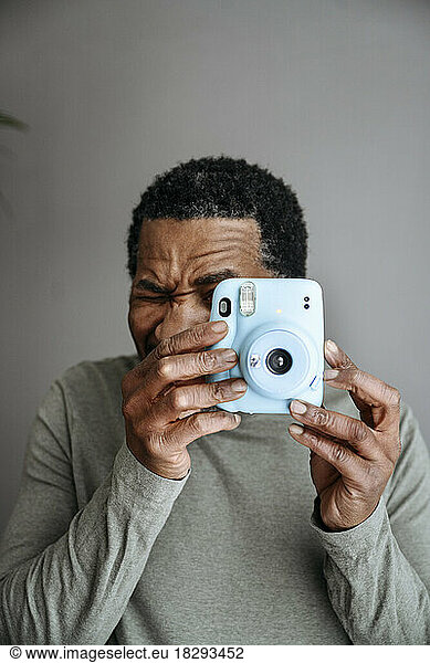 Mature man photographing through instant camera in front of gray wall