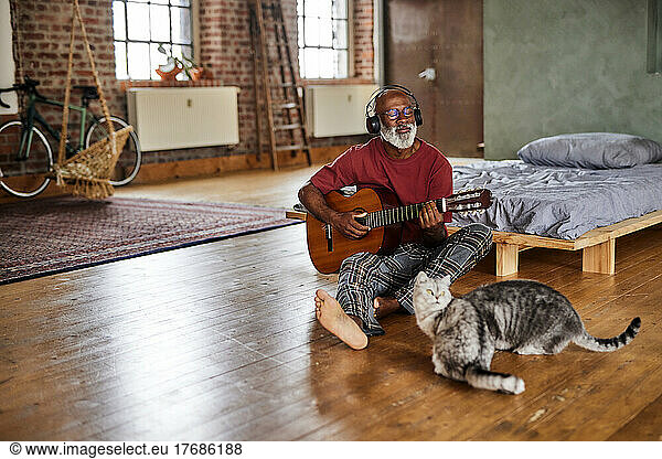 Mature man playing guitar by cats in bedroom at home