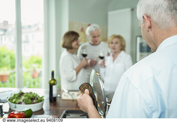 Mature man preparing food while friends drinking wine in background