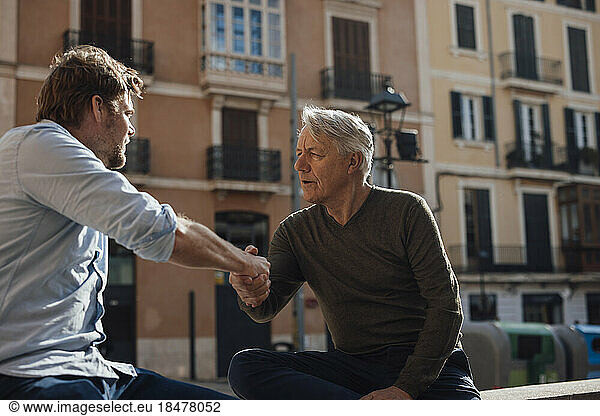 Mature man shaking hands with father sitting in front of building