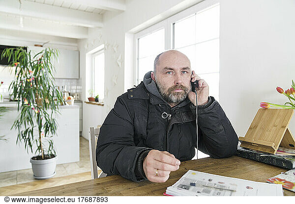Mature man sitting at home wearing winter jacket making a phone call